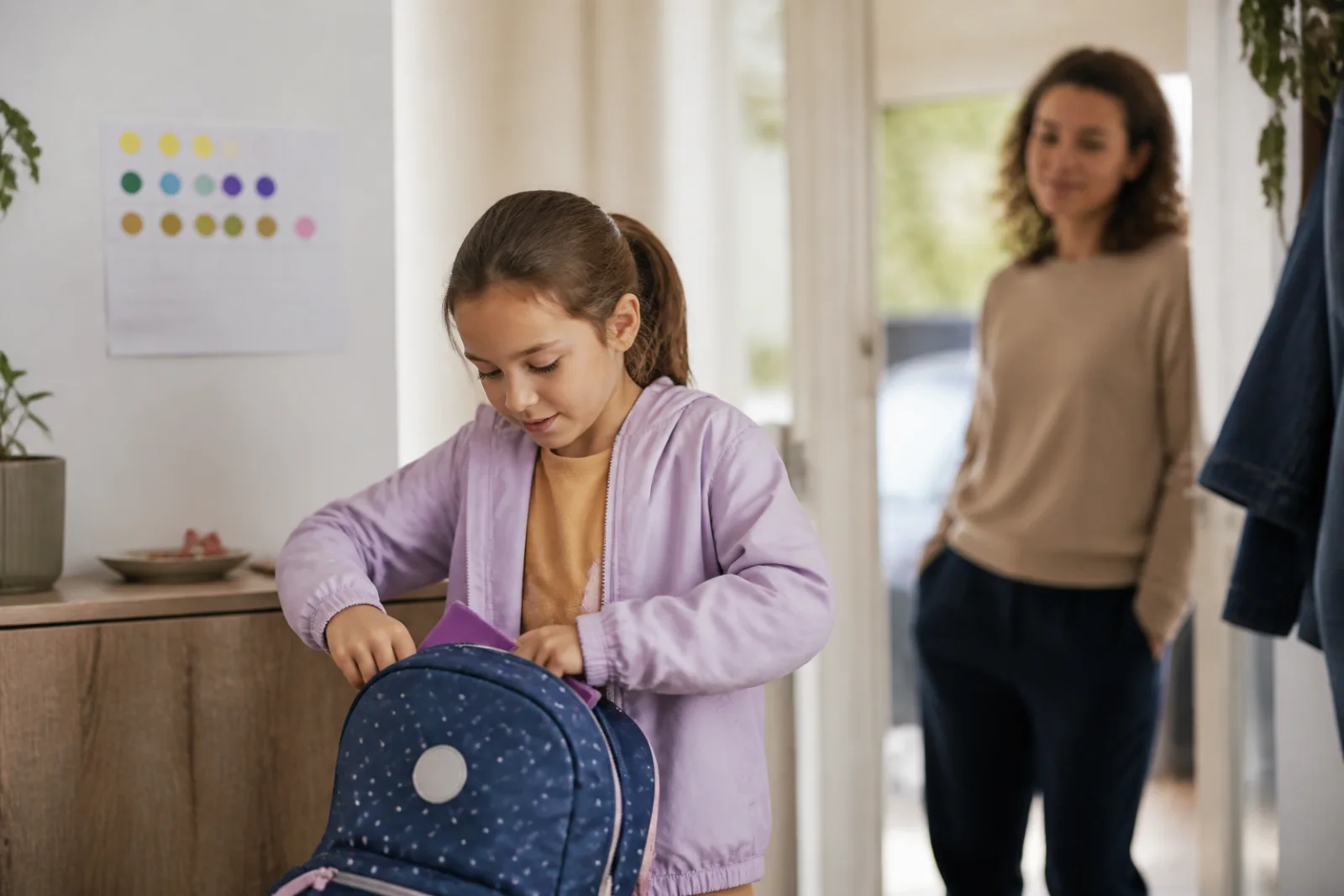 A child independently performs a familiar morning routine while a parent smiles in the background.